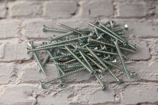 A large group of metallic screws lies haphazardly on a textured brick background, catching the light and highlighting their smooth, polished surfaces. This scene captures the beauty found in everyday