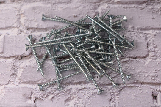A multitude of gleaming metal screws lies haphazardly on a rustic brick surface, reflecting light from nearby tools. This scene captures the essence of craftsmanship and the spirit of DIY projects