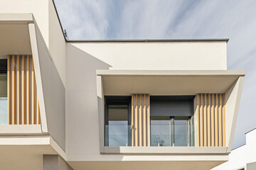 Fototapeta premium Close-up angular view of contemporary building facade with wooden slats, glass railings, and cantilevered balcony