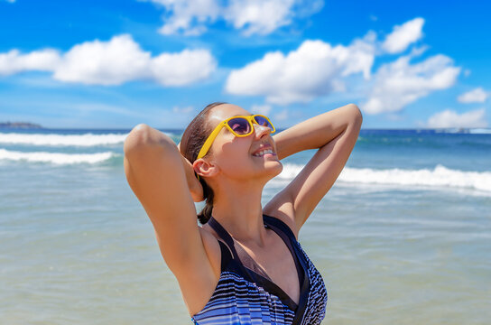 A happy woman wearing yellow sunglasses relaxes on a sunny beach near the ocean.