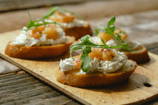 Bruschetta or crostini with cream cheese, shrimp and arugula on wooden board. Tasty snacks.