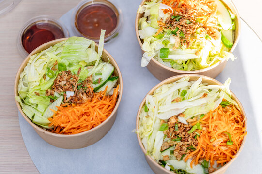 Three Asian noodle salad bowls with fresh vegetables and fried onion topping, top view. Healthy Vietnamese or Asian food concept. Round paper take away containers filled with rice noodles, grated carr