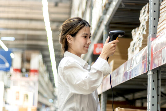 Asian woman worker using laser barcode reader to scan stock inventory in warehouse. Young beautiful female logistic staff scans the barcode of products on shelves in wholesale warehouse.