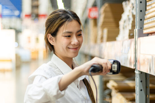 Asian woman worker using laser barcode reader to scan stock inventory in warehouse. Young beautiful female logistic staff scans the barcode of products on shelves in wholesale warehouse.
