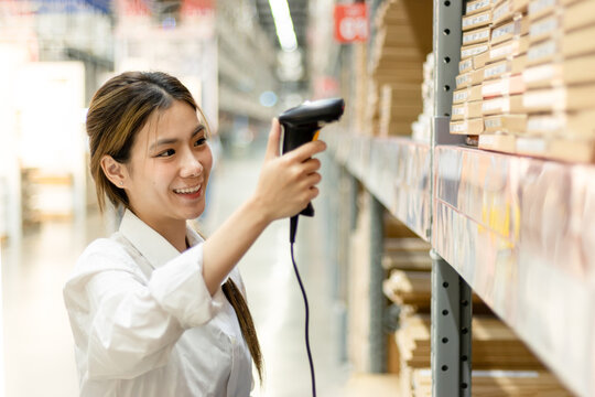 Asian woman worker using laser barcode reader to scan stock inventory in warehouse. Young beautiful female logistic staff scans the barcode of products on shelves in wholesale warehouse.