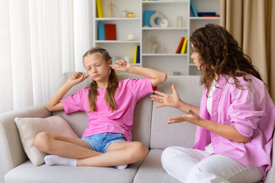 Young daughter closing her eyes and covering her ears while mother speaking and gesturing beside her, illustrating refusal to listen, parental conflict, and emotional tension at home