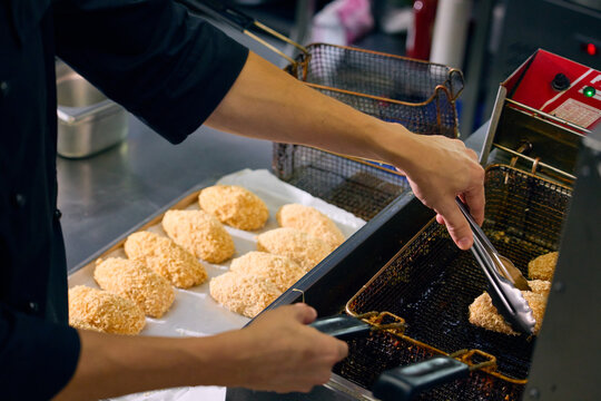 Cook arranging breaded portions with tongs during restaurant kitchen preparation. Concept of food service operations, batch meal preparation, professional kitchen efficiency.