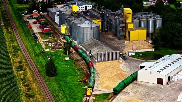 Aerial view of a large industrial grain silo facility with a freight train on tracks and piles of grain in Europe.