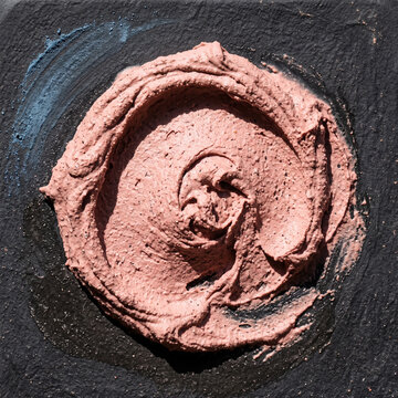 Top view of textured pink clay mask smear on a dark slate surface. Close up of thick cosmetic paste swatch with circular motion. Tactile skincare ingredient