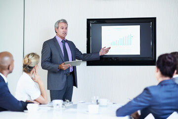 Fototapeta premium Business man, screen and tablet in presentation with team, graphs or revenue info at finance agency. Male speaker, listening and monitor with chart for sales performance, discussion and technology