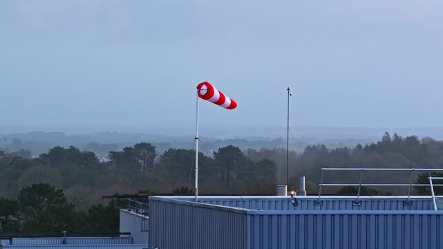 Aerial view of a red and white windsock blowing in the wind on a rooftop with a distant landscape in Europe.