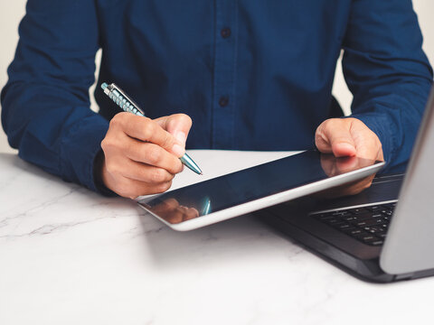 Person Writing on Tablet with Stylus Beside Laptop