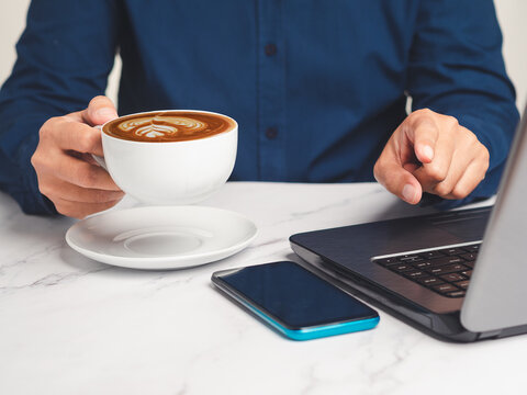 Person Holding Coffee Cup Beside Laptop and Smartphone