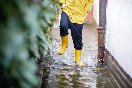 Child splashing through a flooded path in yellow rain boots and a raincoat, enjoying outdoor play during wet weather after heavy rain