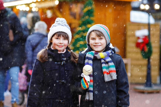 Little cute kid girl and boy eating white chocolate-covered strawberries and apple skewers at German Christmas market. Happy siblings. Real life, real people, snowy festive joy
