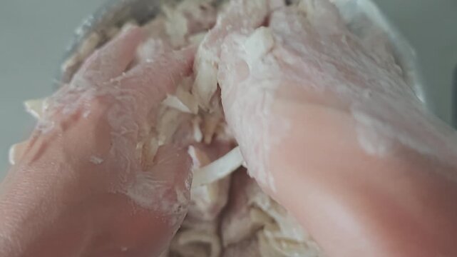 Woman's hands mixing pieces of raw pork meat with onion and marinade sauce in a bowl. Close up view of meal preparation for a barbecue