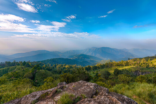 Layered green mountain ridges and forested hills rolling into the haze beneath a bright blue sky