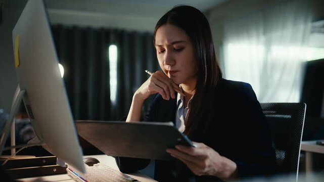 Young Asian professional feeling stressed while working late in the office. Serious businesswoman concentrating on a computer, looking tired
