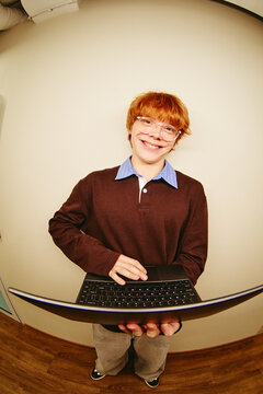 Portrait of Caucasian man holding laptop and smiling, representing technology education, digital learning, and student life, vertical fisheye shot