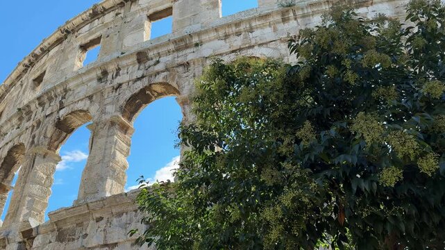 Ancient Roman amphitheater Pula, Croatia features arched openings and a weathered stone facade under a clear blue sky, highlighting its architectural beauty and historical context