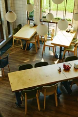 Fotobehang Horeca High angle view of empty modern cafe interior with wooden tables and chairs, showcasing contemporary restaurant design for hospitality marketing, vertical  © Seventyfour