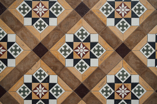 Vintage geometric ceramic floor tile pattern with decorative floral motifs and textured surface.