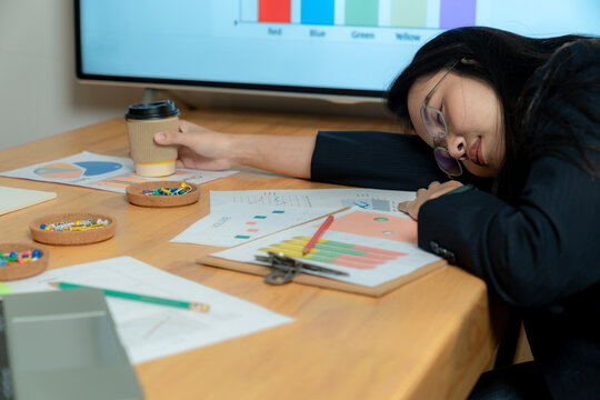 A tired female office worker falls asleep at her desk while working late at night in a quiet corporate office.