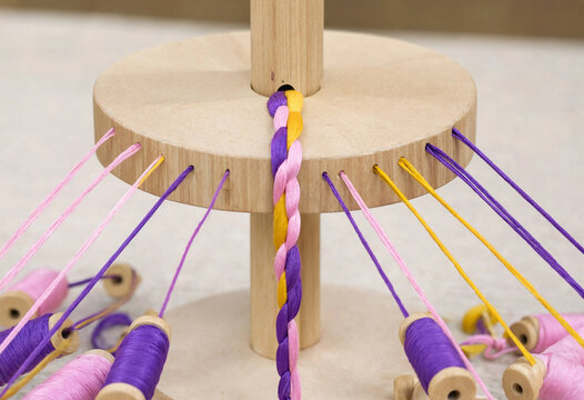 Hands braiding colorful threads on a traditional Japanese kumihimo stand