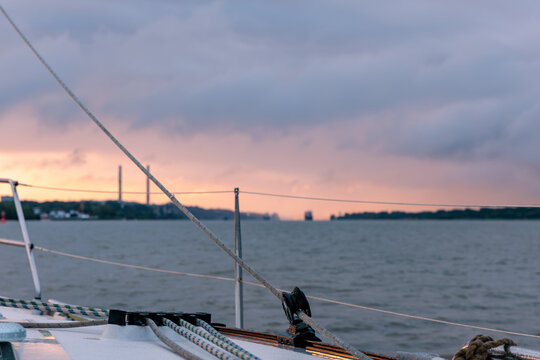View from sailboat deck with rigging, ropes and railing looking out over water during colorful sunset at dusk