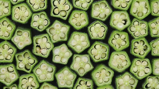 Sliced fresh okra arranged side by side showing seeds slowly rotating on a black background.