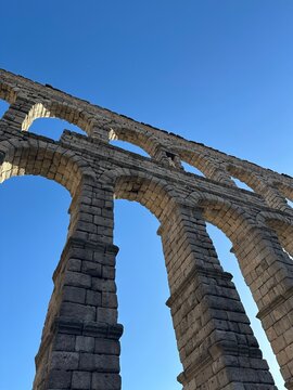 Low angle view of ancient Roman Aqueduct of Segovia stone arches against clear blue sky