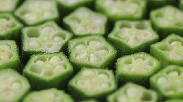 Sliced fresh okra arranged side by side showing seeds slowly rotating on a black background.