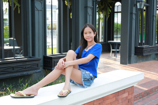 An Asian girl is sitting on a brick ledge and smiling while relaxing in the garden.