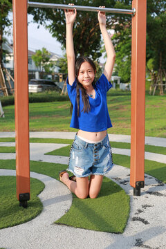 Cheerful young Asian girl holding onto the horizontal bar, enjoying outdoor playtime.