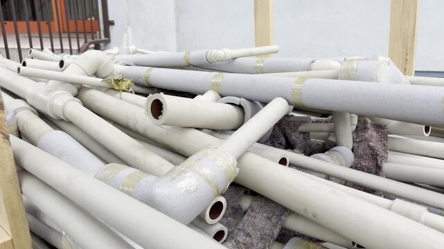 A pile of disassembled plastic water pipes with foam thermal insulation lies stacked outdoors. These plumbing materials are collected and prepared for waste management