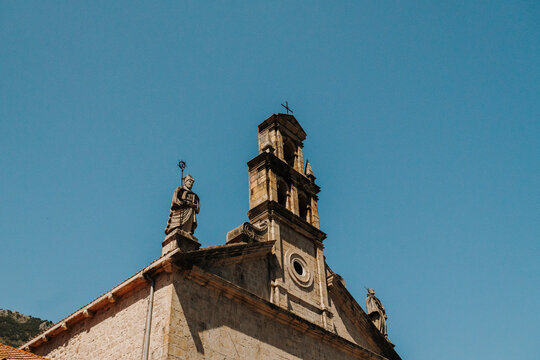 Historic stone church facade with statues and bell tower in Prcanj on the Bay of Kotor. Baroque architecture beneath a clear Mediterranean summer sky