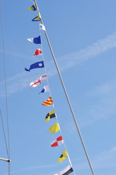 A low angle shot of a white sailboat mast decorated with a string of colorful international maritime signal flags flying under a clear sky.