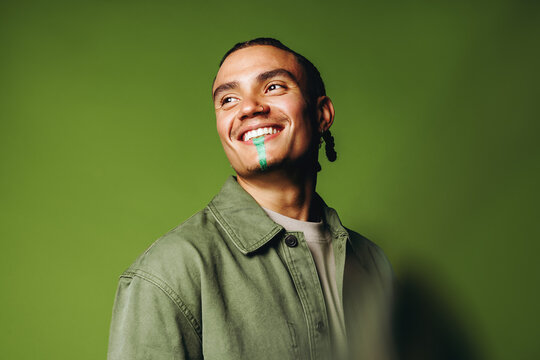 Smiling man in the studio wears artistic face paint with casual fashion