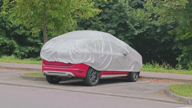 Red modern crossover SUV parked in a lot under a gray protective weather cover. Concept of vehicle storage, safety, and preservation