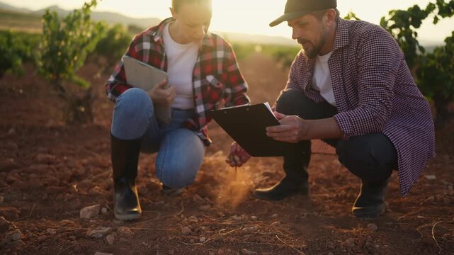 Male and female agricultural specialists examining soil while reviewing digital and printed farm records . Soil analysis, farm planning, sustainable agriculture and crop management concept