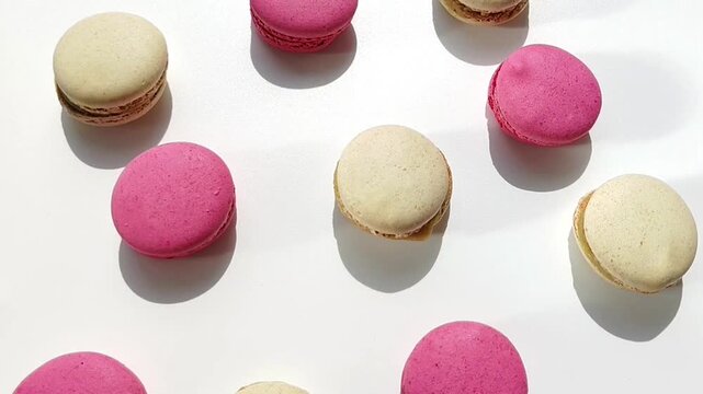 Assorted pink and vanilla macarons arranged on a white surface in studio light. Dessert pattern, bakery, food styling, sweet snack.