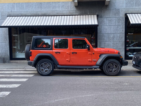 Orange Jeep Wrangler Rubicon sits on a city street, showcasing distinct details and a modern design