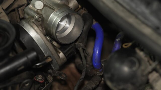 Mechanic installing a blue vacuum hose to car throttle body.