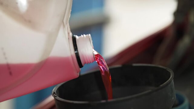 Pouring pink antifreeze coolant liquid from plastic bottle into funnel.