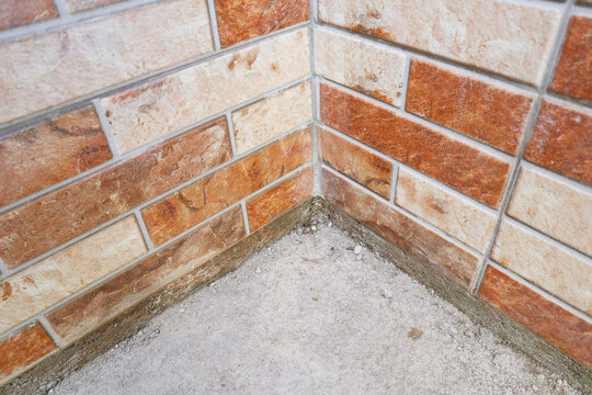 Inside corner view of an orange and beige split-face decorative brick tile wall meeting a concrete floor base