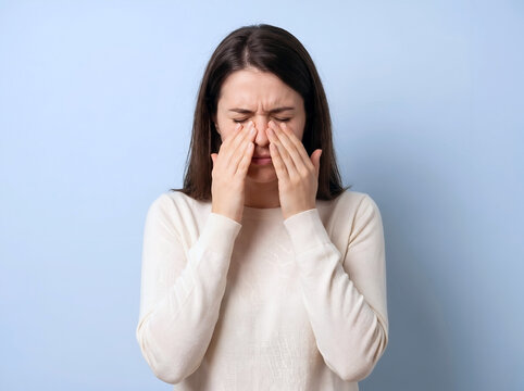 Studio photo of a female pinching her nose bridge with both hands while keeping her eyes tightly shut due to sinus pressure or a severe headache