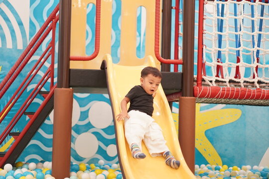 Happy toddler sliding down yellow slide in colorful indoor play center