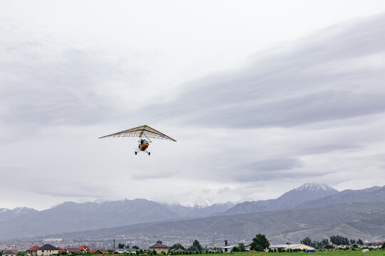 Motorized hang glider ultralight trike flying isolated in gray overcast sky background.