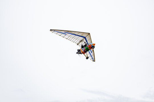 Motorized hang glider ultralight trike flying isolated in gray overcast sky background.