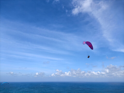 Tandem Paraglider Soaring High Above the Ocean Under Blue Sky